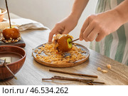 Женщина катит карамельное яблоко в кукурузных хлопьях за деревянным столом. Стоковое фото, фотограф Pixel_shot / Фотобанк Лори