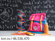 Розовый школьный рюкзак с канцелярскими принадлежностями, молекулярной моделью и бутылкой сока на белом столе рядом с черной меловой доской. Стоковое фото, фотограф Pixel_shot / Фотобанк Лори