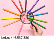 Женская рука с увеличителем и рамкой из разноцветных карандашей на розовом фоне. Стоковое фото, фотограф Pixel_shot / Фотобанк Лори