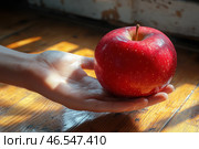 A hand holding a large red apple. The fruit looks fresh, ripe and shiny, and its surface is decorated with tiny light dots. The sunlight falls on the hand and the apple, creating beautiful highlights and emphasizing the texture of the skin and wood in the background.The background is slightly blurred, but you can see the old wooden floor or table with warm tones, which creates a cozy atmosphere. Light and shadows give the image a natural and artistic style. This shot can symbolize fertility, health, temptation or a gift. Стоковое AI-изображение, AI-художник Анна Кривицкая / Фотобанк Лори