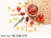 Композиция с плетеной циновкой, миской вкусной томатной пасты и сырой пастой фарфалле на белом гранж-фоне. Стоковое фото, фотограф Pixel_shot / Фотобанк Лори