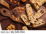 Деревянная доска с вкусным печеньем бискотти, шоколадом, орехами и корицей на фоне ткани, крупным планом. Стоковое фото, фотограф Pixel_shot / Фотобанк Лори