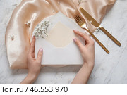 Женщина держит конверт с пустой пригласительной открыткой и цветами гипсофилы возле сервированного стола. Стоковое фото, фотограф Pixel_shot / Фотобанк Лори