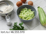 Чашки с тертыми кабачками, мукой и яйцами для приготовления оладий на белом плиточном фоне. Стоковое фото, фотограф Pixel_shot / Фотобанк Лори