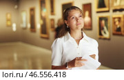 Young girl holding an information booklet looks at paintings in an art exhibition in a museum. Стоковое видео, видеограф Яков Филимонов / Фотобанк Лори