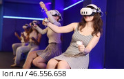 Four cheerful emotional young female friends in VR goggles sitting in virtual reality room, manipulating objects or shooting at targets with gaming controllers in hands. Стоковое видео, видеограф Яков Филимонов / Фотобанк Лори