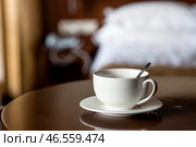 A white cup of hot tea or coffee on a wooden table in the interior of a hotel room. The concept of drinks and comfortable hotel accommodation. Стоковое фото, фотограф Photojuli / Фотобанк Лори