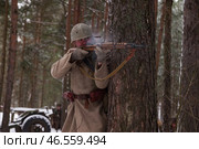 Sestroretsk, Russia - February 19, 2023: Capturing the essence of a winter battlefield, a soldier takes cover behind a tree, engaged in combat. Редакционное фото, фотограф Aleksandr Golubev / Фотобанк Лори