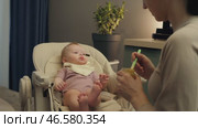 Mother Spoon-Feeding Infant Girl Vegetable Puree in a Highchair. Стоковое видео, видеограф Михаил Матвеев / Фотобанк Лори
