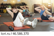 Concentrated young man doing abdominal exercise on yoga mat during group workout in gym. CrossFit healthy concept. Стоковое фото, фотограф Яков Филимонов / Фотобанк Лори
