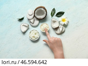 Женская рука с кокосовым маслом в мисках и цветком плюмерии на светло-голубом фоне. Стоковое фото, фотограф Pixel_shot / Фотобанк Лори