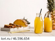 Свежий спелый ананас и бутылки вкусного сока на плиточном столе возле белой стены. Стоковое фото, фотограф Pixel_shot / Фотобанк Лори