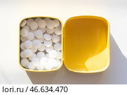 Открытая желтая жестяная коробочка с белыми мятными леденцами на белом фоне. Стоковое фото, фотограф Anton Leonchikov / Фотобанк Лори