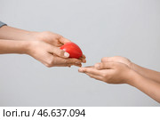 Женщина дает маленькому ребенку маленькое красное сердце хо на сером фоне. Концепция пожертвований. Стоковое фото, фотограф Pixel_shot / Фотобанк Лори