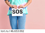 Молодая женщина, держащая бумаги с текстом SOS на цветном фоне. Концепция менструации. Стоковое фото, фотограф Pixel_shot / Фотобанк Лори