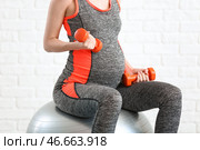 Красивая беременная женщина с гантелями и фитболом у белой кирпичной стены. Стоковое фото, фотограф Pixel_shot / Фотобанк Лори