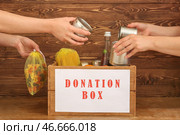 Добровольцы кладут еду в ящик для пожертвований на деревянном фоне. Стоковое фото, фотограф Pixel_shot / Фотобанк Лори