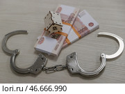 Банкноты номиналом 5000 российских рублей, деревянный домик и наручники на столе. Стоковое фото, фотограф Сергей Булкин/NEWS.ru / ТАСС / Фотобанк Лори
