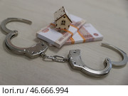 Банкноты номиналом 5000 российских рублей, деревянный домик и наручники на столе. Стоковое фото, фотограф Сергей Булкин/NEWS.ru / ТАСС / Фотобанк Лори