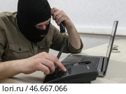 Мошенник в черной балаклаве у ноутбука с телефонной трубкой в руке. Стоковое фото, фотограф Сергей Булкин/NEWS.ru / ТАСС / Фотобанк Лори