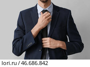 Молодой бизнесмен в костюме устраивает галстук на светлом фоне, крупным планом. Стоковое фото, фотограф Pixel_shot / Фотобанк Лори
