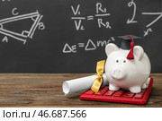 Копилка в форме выпускного берета с дипломом и калькулятором на коричневом деревянном столе перед меловой доской. Концепция студенческого займа. Стоковое фото, фотограф Pixel_shot / Фотобанк Лори