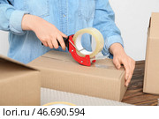 Женщина упаковывает картонную коробку с клеевым ленточным диспенсером за деревянным столом. Стоковое фото, фотограф Pixel_shot / Фотобанк Лори