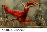 A graceful woman with bright red hair, soaring in a jump above the roofs of a gothic city. She is dressed in a fluttering scarlet dress, emphasizing her swiftness and passion. The wind picks up her light fabric, creating a feeling of movement and weightlessness. The background is made in dark, dramatic tones, with the majestic architecture of ancient buildings, which enhances the contrast with her fiery image. Autumn leaves swirl around her, as if emphasizing the moment of freedom and emotional uplift. The picture is filled with expression, dynamics and symbolism. Стоковое AI-изображение, AI-художник Анна Кривицкая / Фотобанк Лори