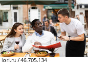 On open area of cafe, guy waiter communicates with multiethnic couple of customer, accepts order. Стоковое фото, фотограф Яков Филимонов / Фотобанк Лори
