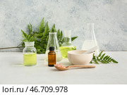 Бутылка с маслом, лабораторная стеклянная посуда с образцами и ингредиентами для приготовления натуральной косметики на белом столе рядом с шероховатой стеной. Стоковое фото, фотограф Pixel_shot / Фотобанк Лори