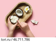 Женские руки с кокосовым маслом в скорлупе и цветком плюмерии на розовом фоне. Стоковое фото, фотограф Pixel_shot / Фотобанк Лори