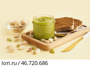 Деревянный поднос с банкой фисташковой пасты, ложкой и хлебом на бежевом фоне. Стоковое фото, фотограф Pixel_shot / Фотобанк Лори