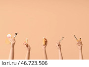 Женские руки с флаконом сыворотки, плойкой, хайлайтером, тушью для ресниц, консилером и кистью на бежевом фоне. Стоковое фото, фотограф Pixel_shot / Фотобанк Лори