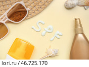 Композиция с бутылками солнцезащитного крема, солнцезащитными очками, шляпой и словом SPF, написанным кремом на бежевом фоне. Стоковое фото, фотограф Pixel_shot / Фотобанк Лори