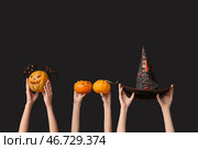 Женская рука с тыквами, ободок с крыльями летучей мыши и ведьминой шляпой на черном фоне. Празднование Хэллоуина. Стоковое фото, фотограф Pixel_shot / Фотобанк Лори