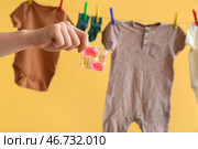 Женская рука с гелевой капсулой для стирки и одежда, висящая на веревке для белья на желтом фоне. Стоковое фото, фотограф Pixel_shot / Фотобанк Лори