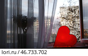 Red heart-shaped lamp stands at window and glows to bestow love on everyone. Стоковое фото, фотограф David Kashakhi / Фотобанк Лори