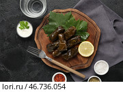 Деревянная доска с вкусными долмами (фаршированные виноградные листья), сметаной, специями и стаканом воды на темном фоне. Стоковое фото, фотограф Pixel_shot / Фотобанк Лори