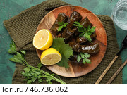 Деревянная тарелка с вкусными долмами (фаршированные виноградные листья), лимоном и петрушкой на цветном фоне. Стоковое фото, фотограф Pixel_shot / Фотобанк Лори