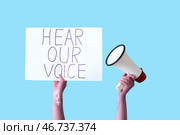 Женщина держит плакат с надписью "УСЛЫШЬТЕ НАШ ГОЛОС" и мегафон на синем фоне. Концепция феминизма. Стоковое фото, фотограф Pixel_shot / Фотобанк Лори