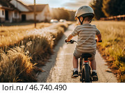 A cheerful little boy rides a bicycle in a helmet outdoors. A happy child is engaged in an active sport. Protection. Life insurance and child safety. Стоковое AI-изображение, AI-художник Photojuli / Фотобанк Лори