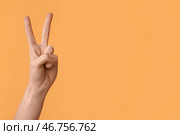 Женская рука, показывающая жест мира на оранжевом фоне, крупным планом. Стоковое фото, фотограф Pixel_shot / Фотобанк Лори