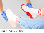 Доктор в медицинских перчатках подбирает ортопедические стельки на женские стопы, изолированные на белом фоне. Стоковое фото, фотограф Pixel_shot / Фотобанк Лори