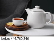 Доска с чашкой горячего заваренного чая, ломтиками лимона и чайником на столе на фоне черного размытого фона. Стоковое фото, фотограф Pixel_shot / Фотобанк Лори