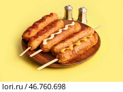 Деревянная тарелка с вкусными корн-догами и различными соусами на желтом фоне. Стоковое фото, фотограф Pixel_shot / Фотобанк Лори