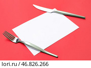 Пустая карточка, нержавеющая стальная вилка и нож на красном фоне, крупным планом. Стоковое фото, фотограф Pixel_shot / Фотобанк Лори