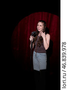 A young woman in jeans and a T-shirt stands behind a microphone on stage and tells stories. Stand-up comedian on stage. Стоковое фото, фотограф Кашапова Эльвира / Фотобанк Лори