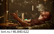 Brutal man smokes cigar. Media. Attractive man with beard smokes cigar coolly. Cinematic cigar smoking with brutal man in restaurant. Стоковое фото, фотограф Данил Руденко / Фотобанк Лори