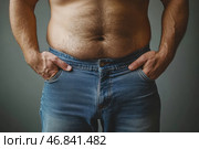 A man with a slightly protruding belly, dressed in jeans. He keeps his hands in his pockets, and his torso remains naked, demonstrating the natural texture of the skin and a small amount of hair on the belly. The lighting is soft, the background is neutral, creating an emphasis on the figure. The photo emphasizes the naturalness of the body, its imperfections and reflects the theme of fullness, excess weight or just a relaxed lifestyle. Стоковое AI-изображение, AI-художник Анна Кривицкая / Фотобанк Лори