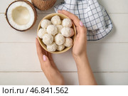 Женщина держит чашу с кокосовыми конфетами на белом деревянном столе. Стоковое фото, фотограф Pixel_shot / Фотобанк Лори